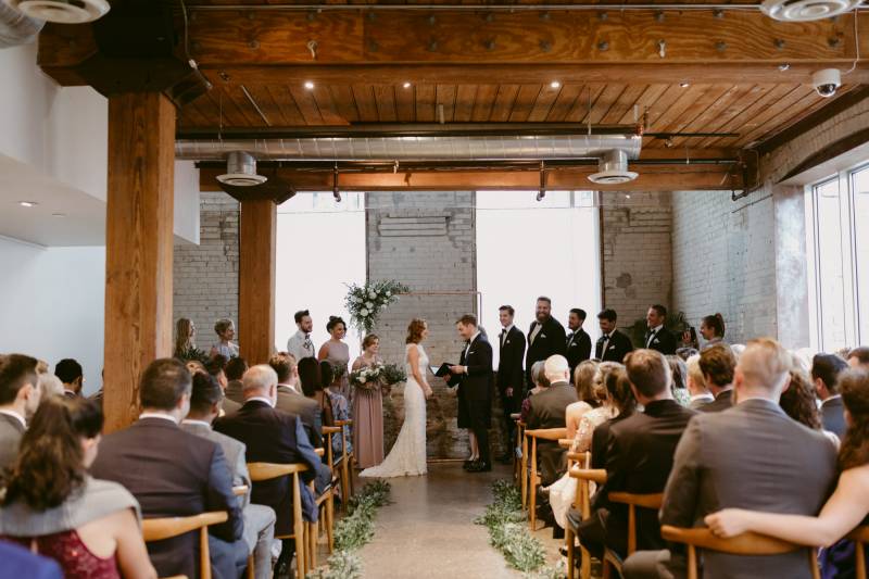 Wedding ceremony with guests to side as officiant reads groomsmen and bridesmaids behind bride and groom 