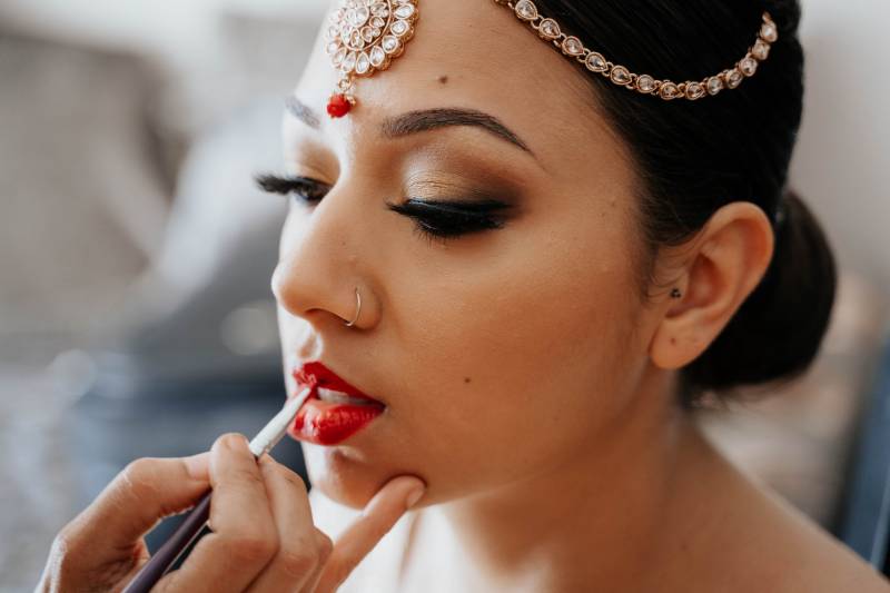 Makeup artist applying red makeup to woman in bridal head jewelry 
