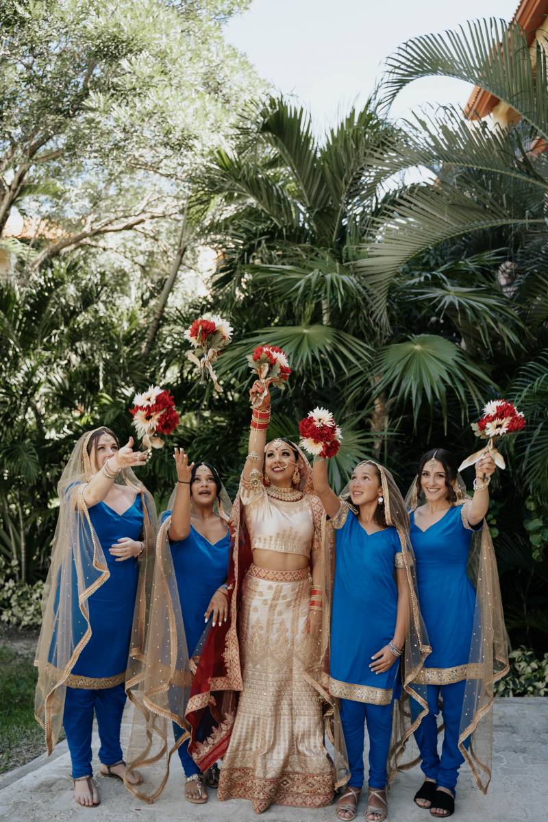 Bride and bridesmaids stand in line holding crimson and white bouquets above heads