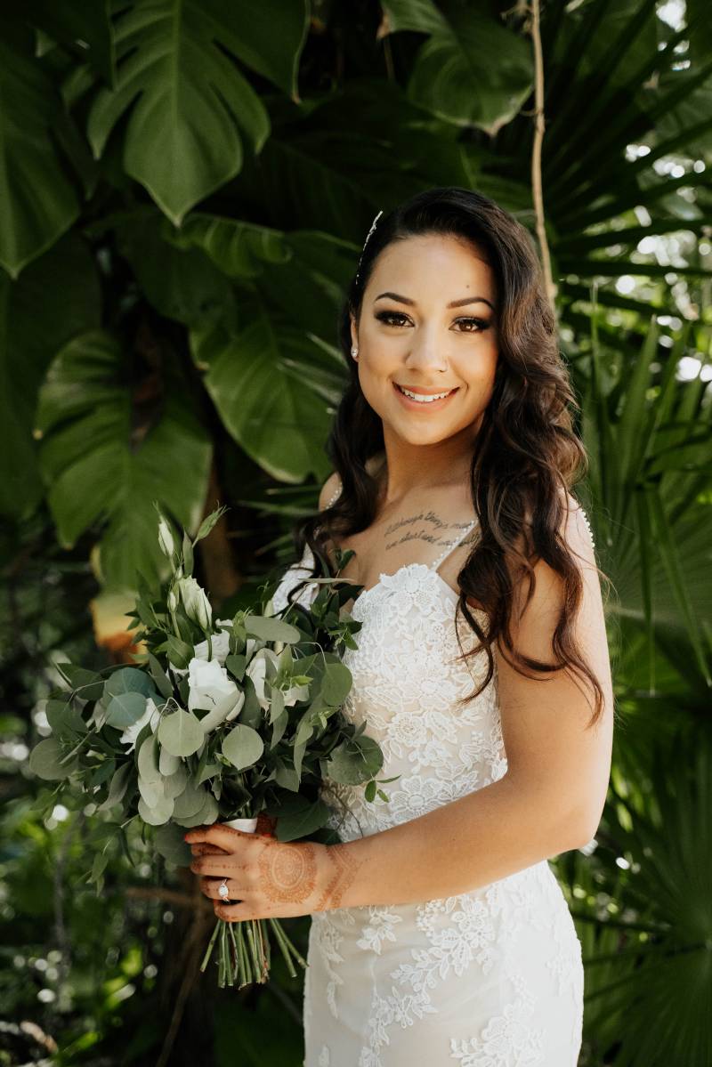 Bride standing smiling in white lace dress holding white bouquet 