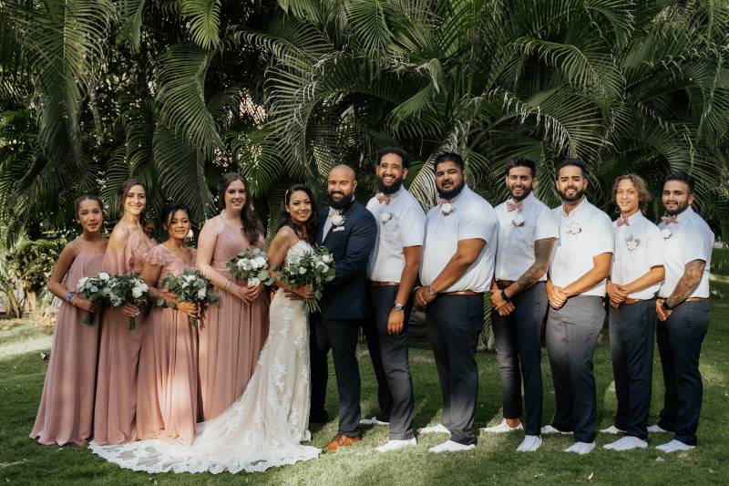 Bride and groom stand in between bridesmaids and groomsmen in line on grass