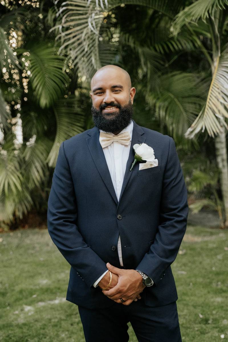 Groom stands arms crossed in front smiling in dark blue suit 