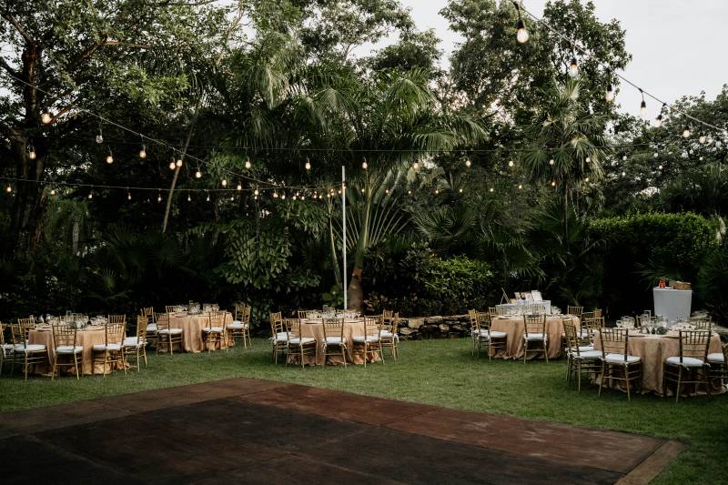 Outdoor wedding reception with hanging lights and circle tables surrounding wood patio 