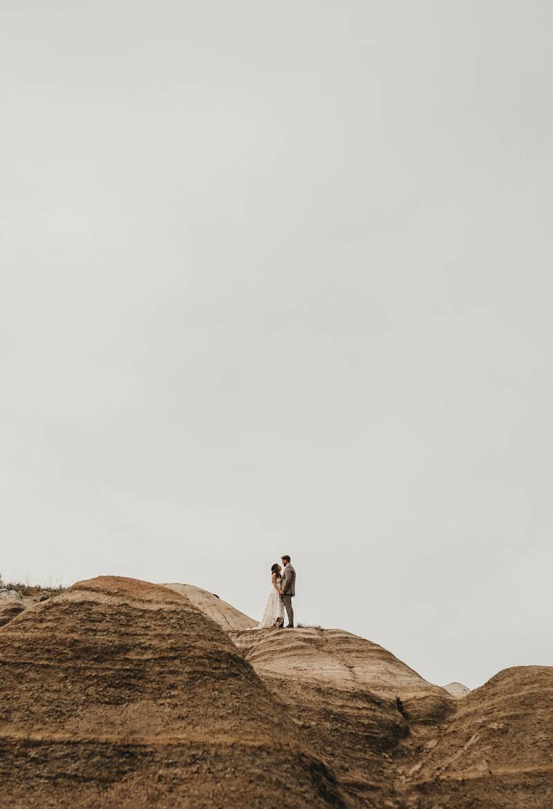 Man and woman stand embraced at top of large dirt hill 