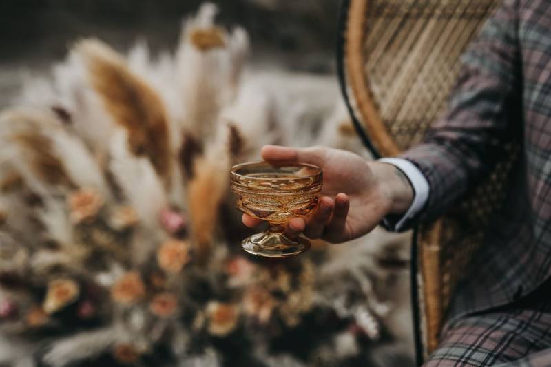 Man holding small glass out sitting in wicker chair 