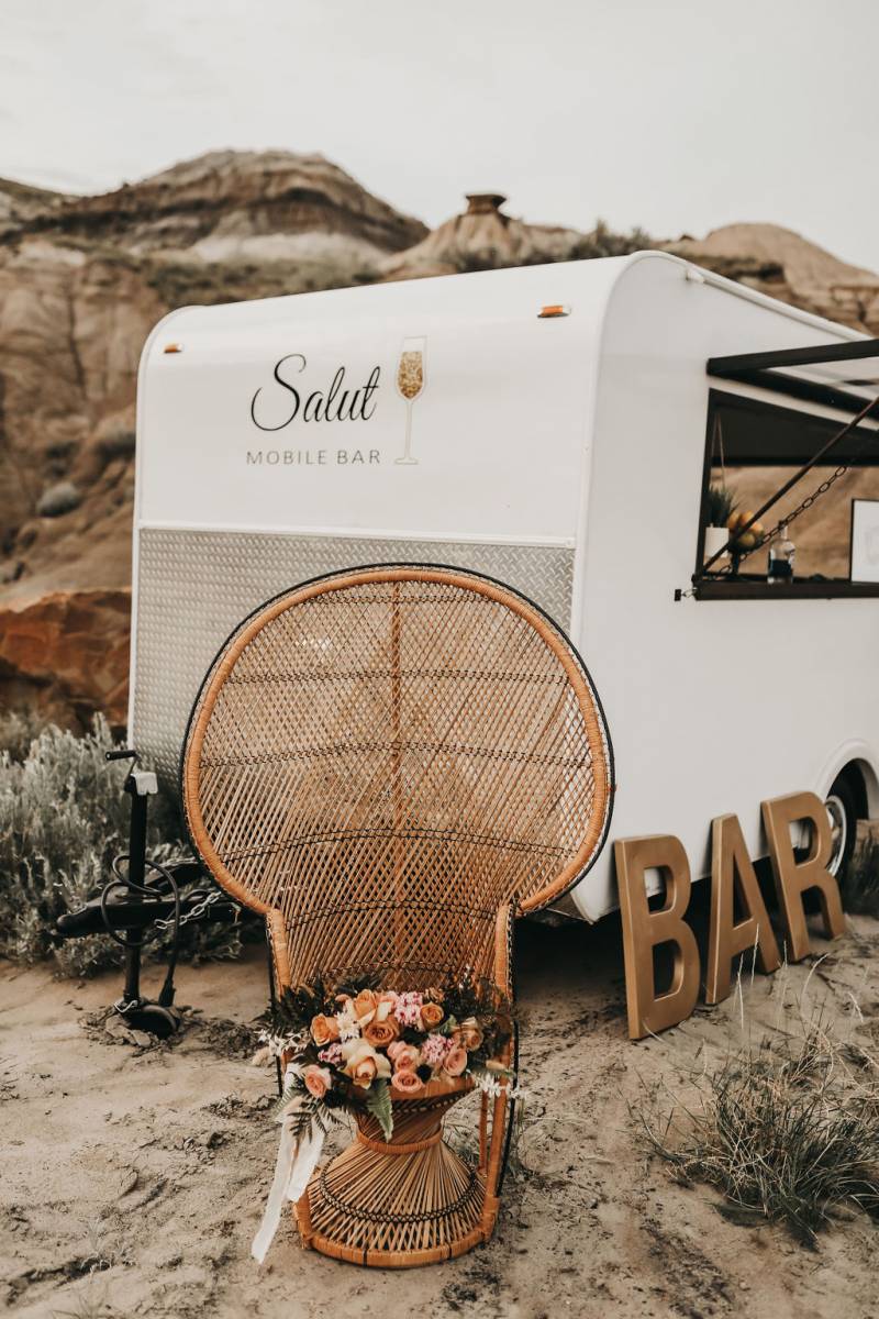 Wicker seat with pale pink and orange bouquet on top with mobile bar behind