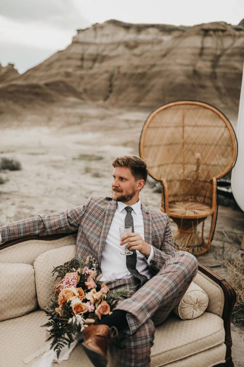 Man in beige suit sits cross legged on couch in desert 
