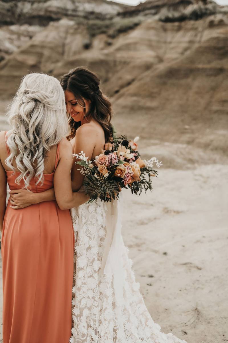 Two women touch foreheads holding bouquet in desert smiling 