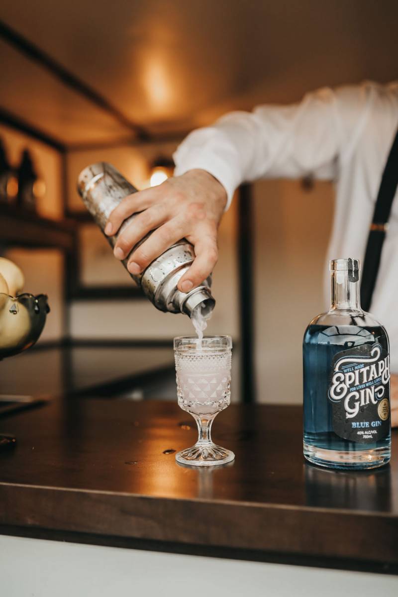 Bartender pouring drink into glass beside bottle of gin 