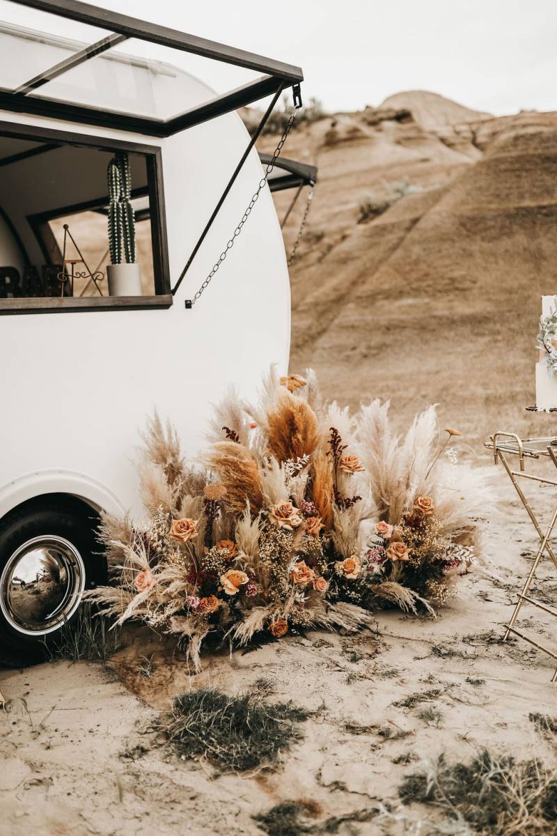 pampas grass floral arrangement sitting on dirt ground beside mobile bar