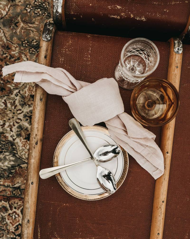 Table setting with large beige tied napkin and glasses on top of brown luggage