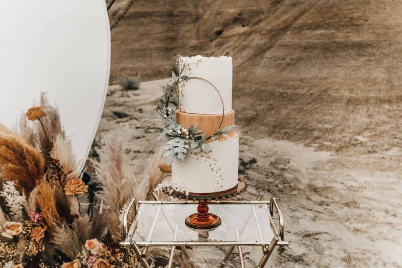 Large white wedding cake sitting on glass table beside pampas grass floral arragement