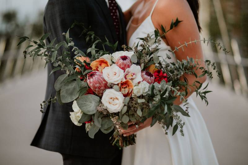 Bride and groom embracing holding orange pink white bouquet 