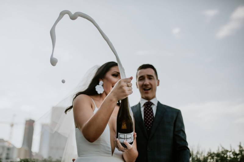 Bride and groom watch foam shoot from glass bottle in arc