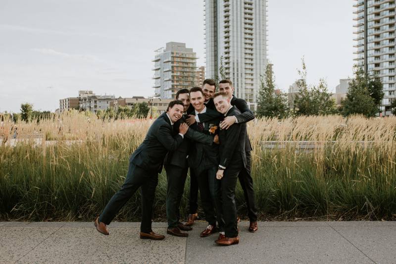 Groom laughing with groomsmen surrounding and embracing him 