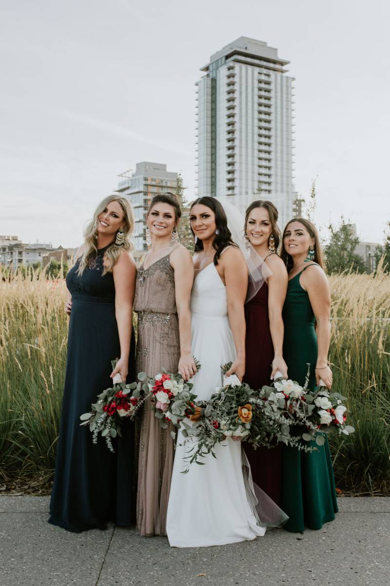 Bride and bridesmaids stand together holding bouquet at side on pathway 