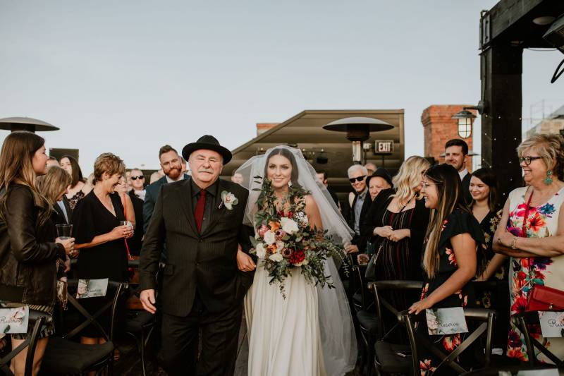 Bride in white dress and white veil holding bouquet walks in arms with man in black suit 