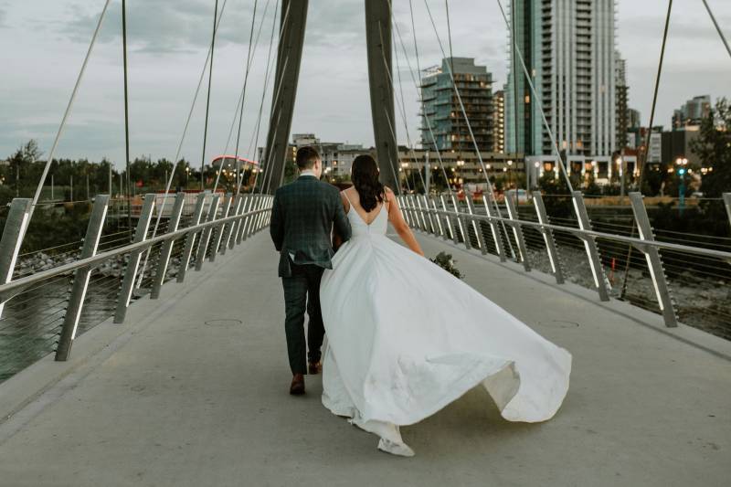 Bride in flowing white dress walking with groom over bridge 