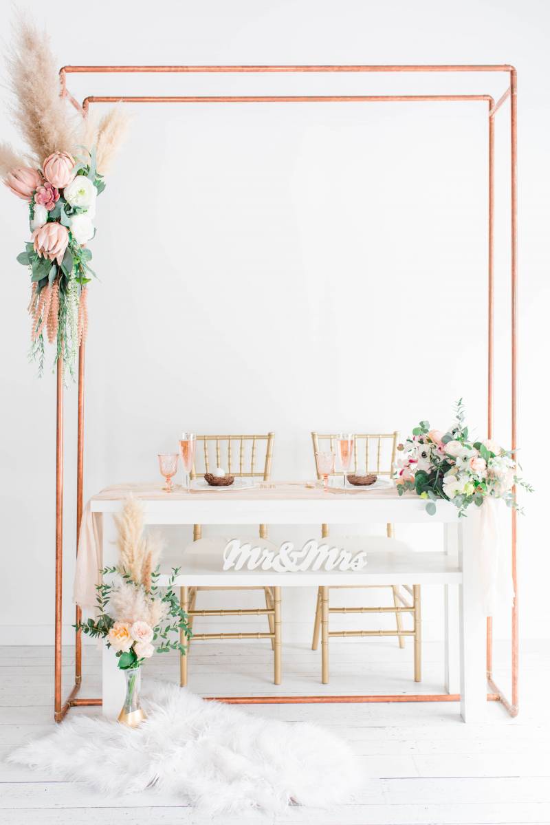 Copper pipe wedding arch with blush and white floral accents and white table 