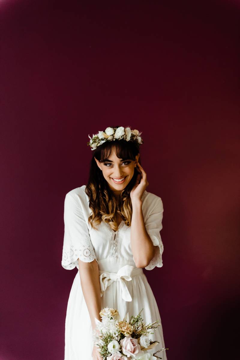 Bride smiling in white dress and white flower crown holding white and blush bouquet 