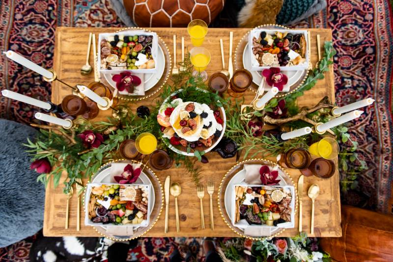 Table setting flat lay with green and maroon table runner and gold cutlery on red shag carpet 