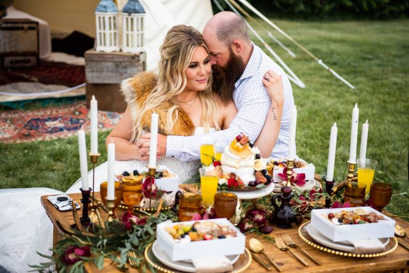 Man and woman embrace sitting behind boho table scape and candle set table 
