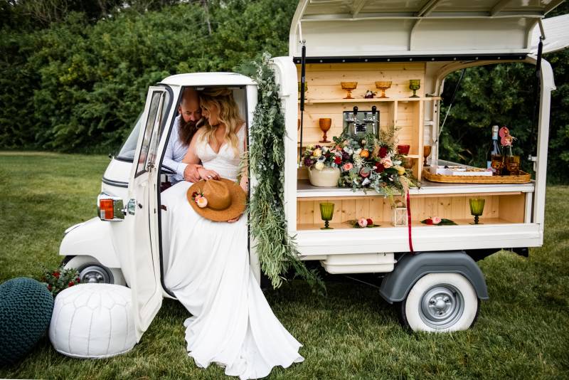 Man and woman in large white dress sit together in open food truck in field 