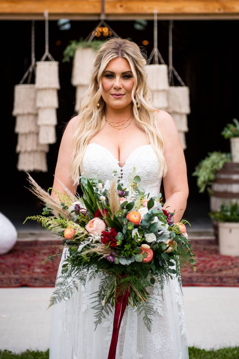 Woman in white lace dress holding large white pink orange and maroon bouquet