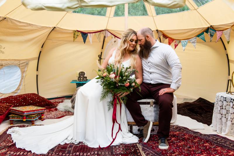 Man and woman touching foreheads sitting in white boho inspired tent 