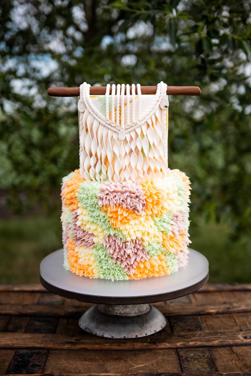 yellow orange pink and green boho wedding cake with macrame decoration on wood table 