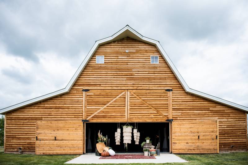 Large wooden barn with hanging macramé and poofs in front of open doorway 