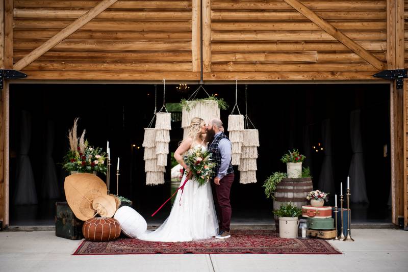 Woman in large white dress holding bouquet kissing man in front of hanging macrame chandeliers 
