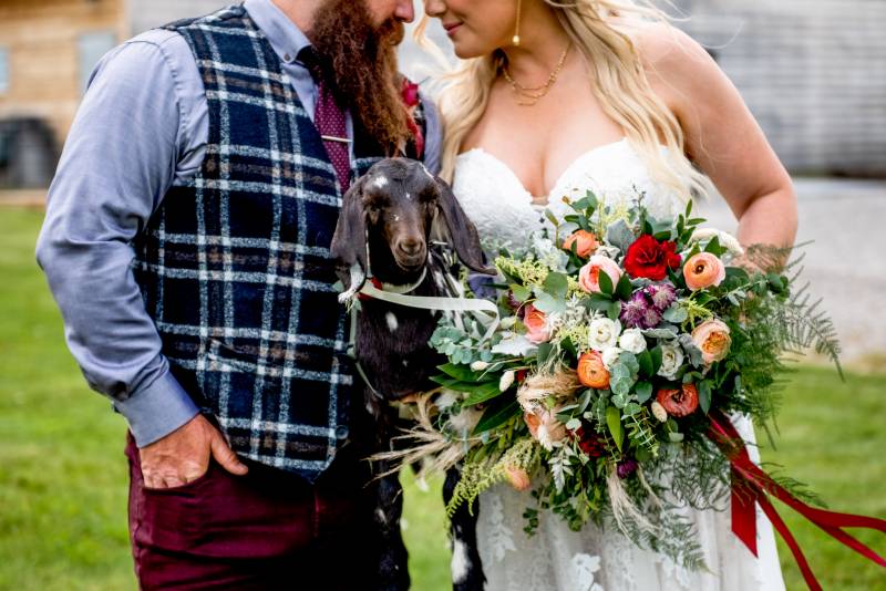 Man and woman holding goat and bouquet touching foreheads