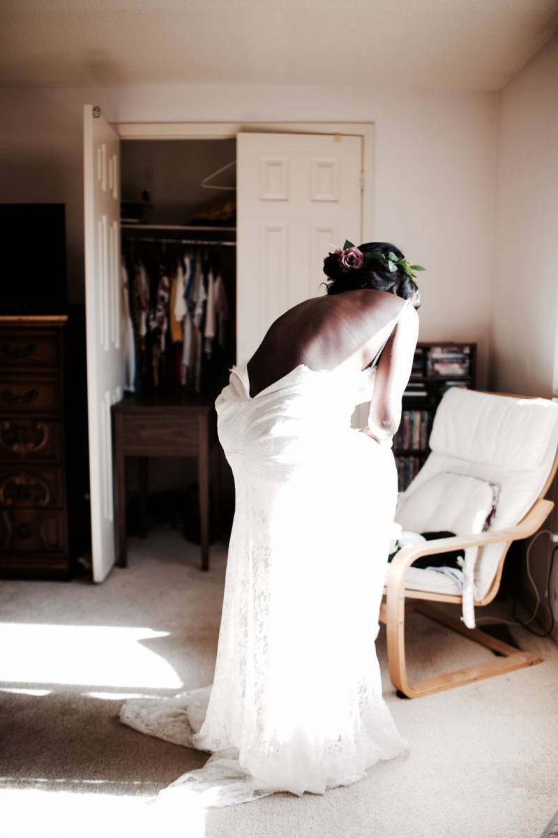 Bride in white open back dress leans over chair 