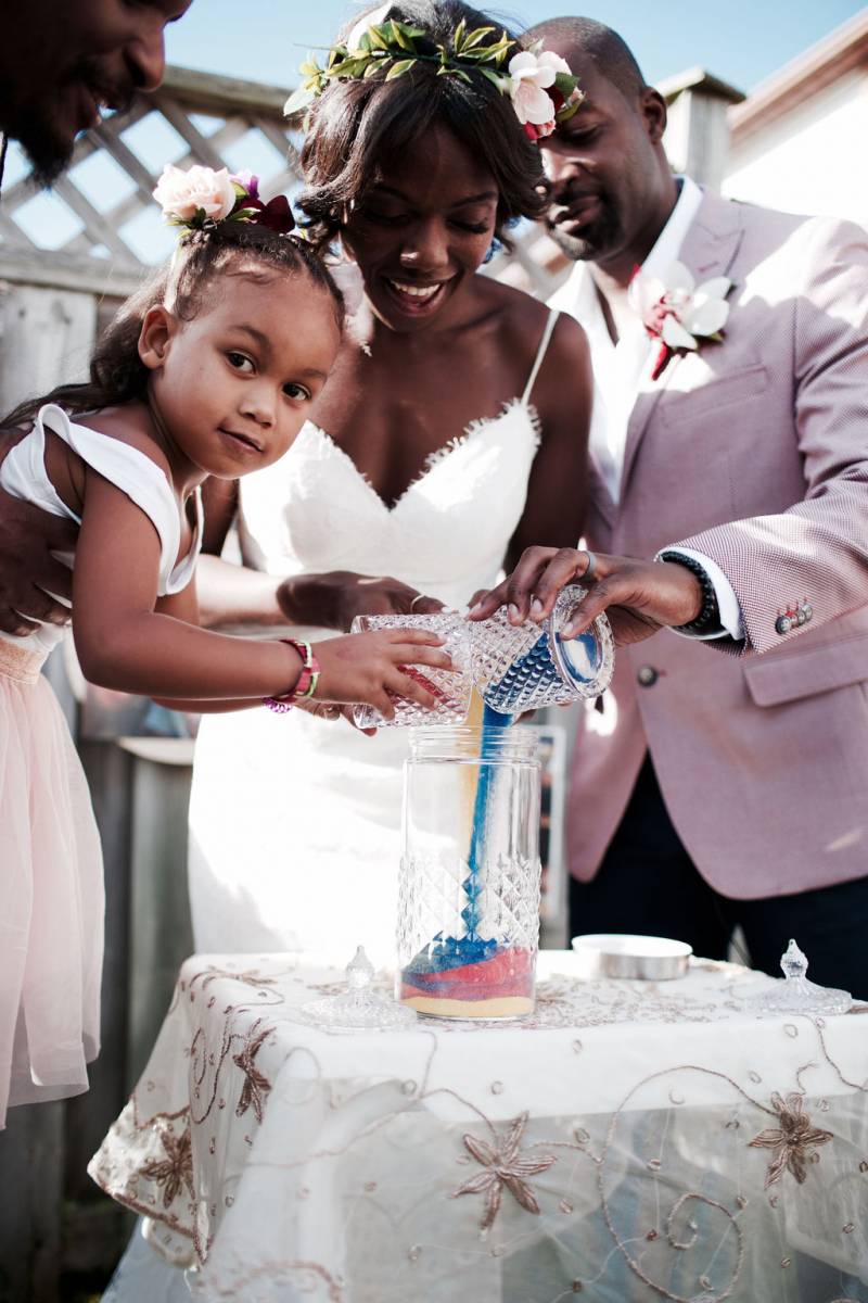 Bride groom and flower girl pour colored sand into glass vase