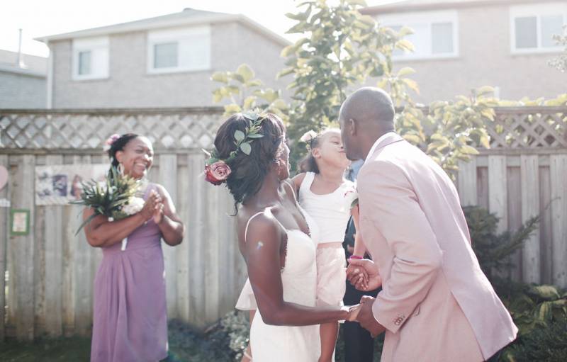 Groom kisses flower girl being held by bride 