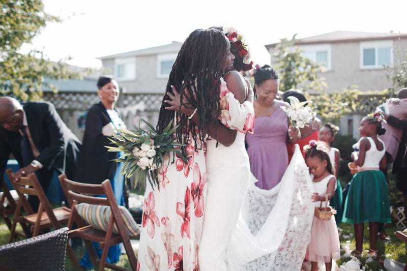 Bride embraced by woman while flower girl lifts lace skirt 