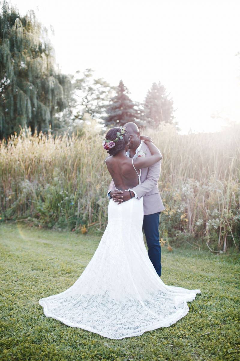 Bride in large white lace dress and groom embrace in grassy field