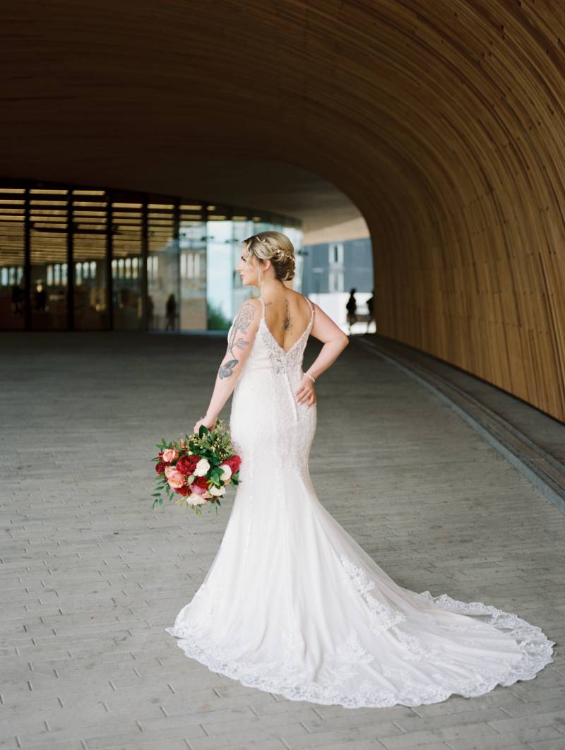 Bride walking in white lace dress holding red peach and white bouquet to side 