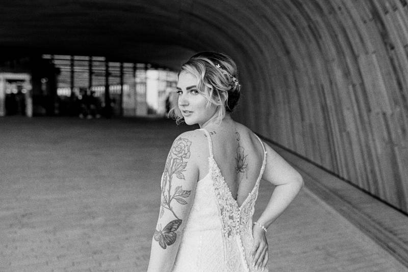 Bride looks over shoulder in white lace open back dress hand on hip black and white 