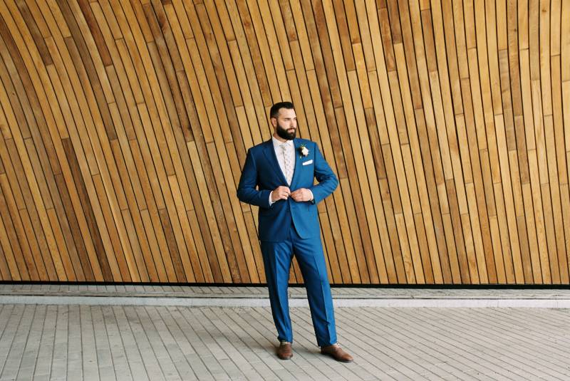 Groom in dark blue suit buttons jacket looking off to side 