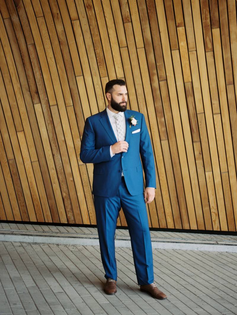 Groom in blue suit holds jacket looking off to side 