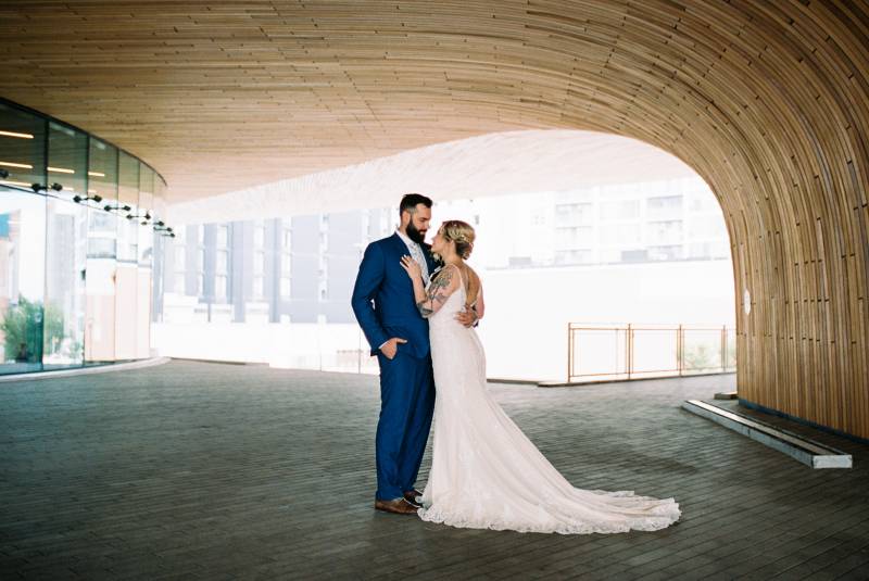 Bride and groom smile while embraced under wooden arch 