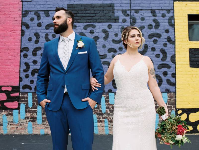 Bride and groom stand looking opposite directions against painted brick building 