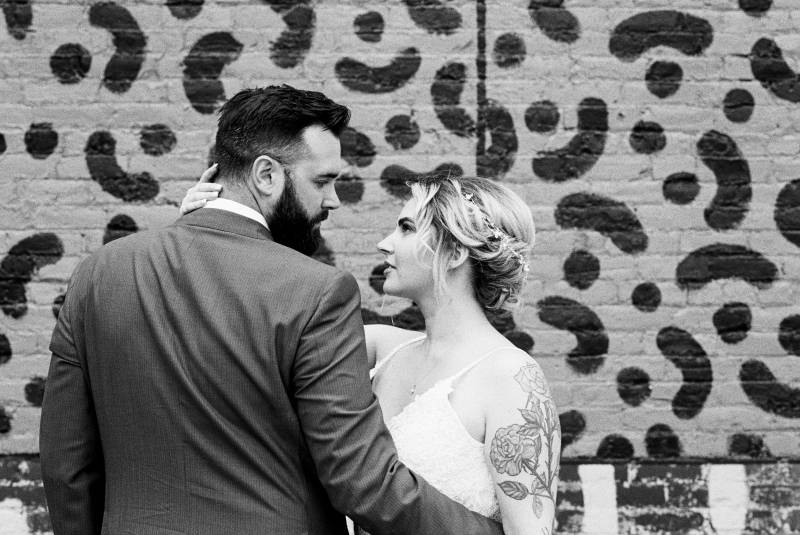 Bride and groom stare intensely against brick wall black and white 