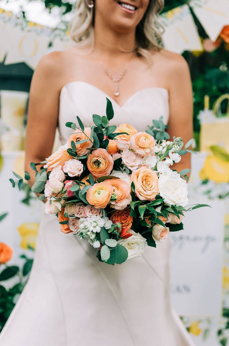 Bride in white dress holding peach bouquet with white flowers 