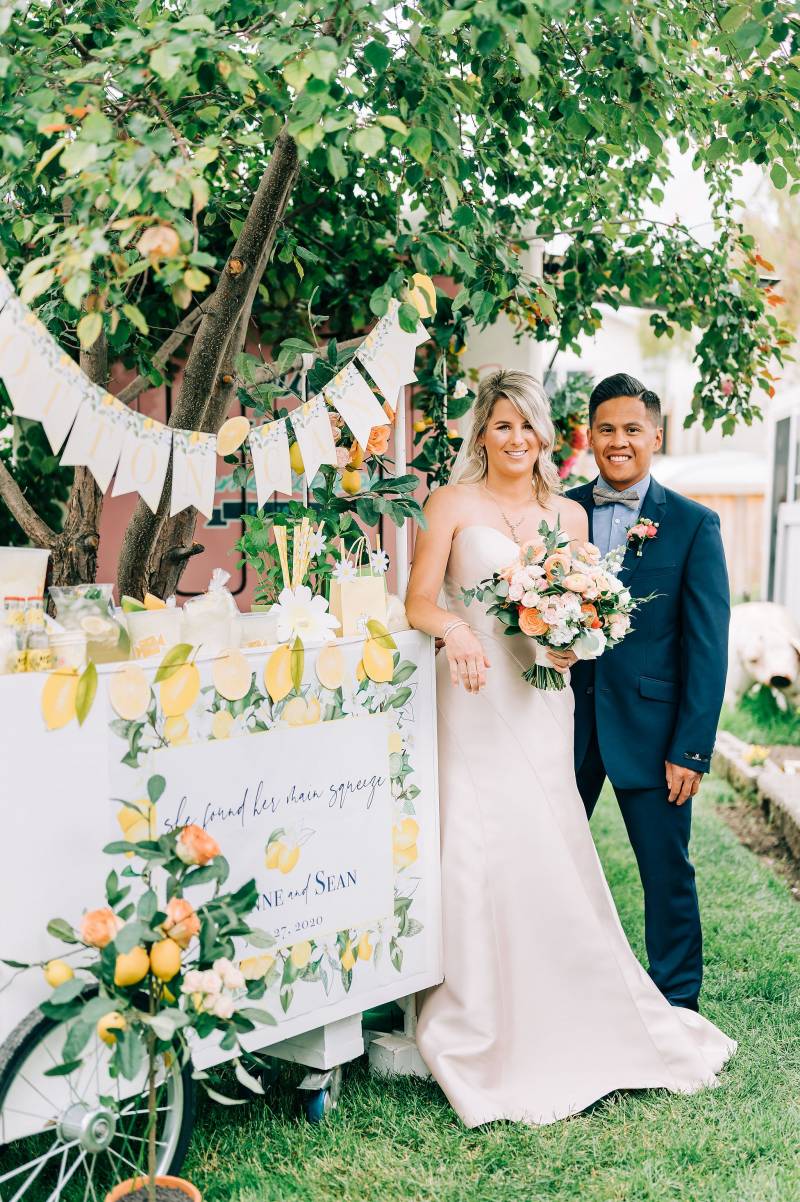 Bride holding bouquet standing next to groom leaning against trolley lemonade stand 