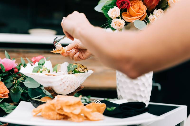 Hands applying dip to chip beside floral arrangement on table 