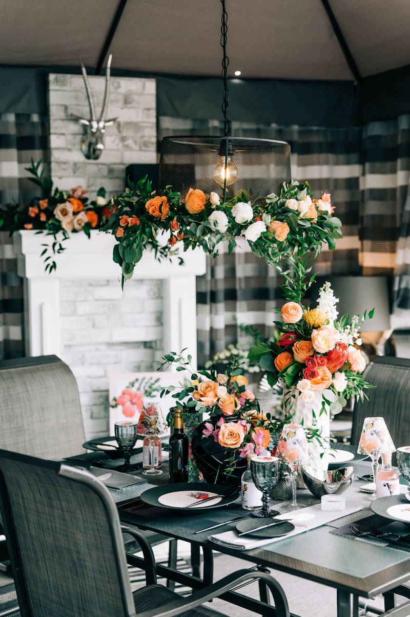 Small table with large floral centerpiece and hanging chandelier by white fireplace 