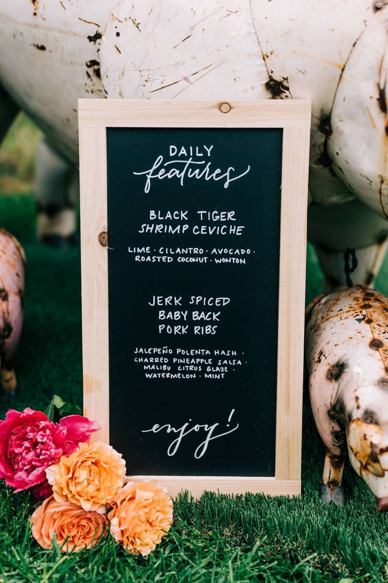 Wedding reception menu on chalkboard beside flowers on grass